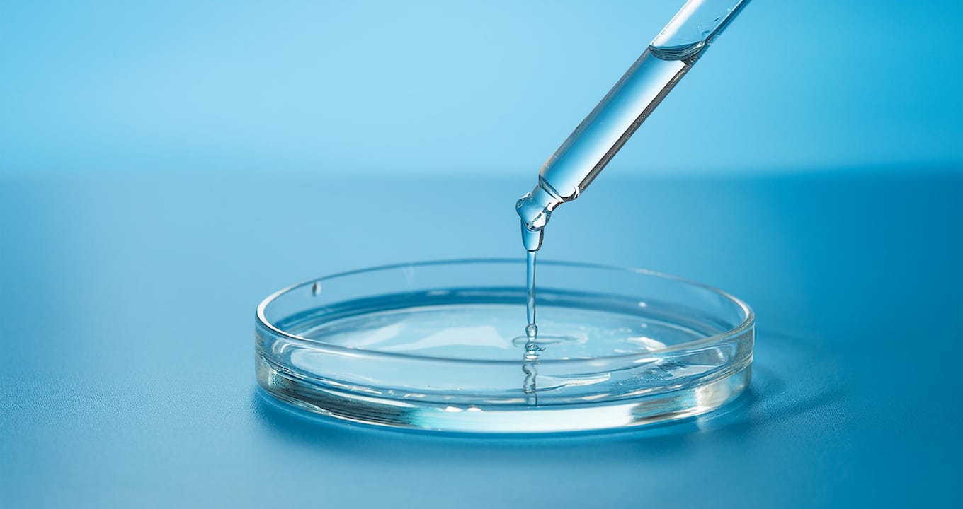 A clear liquid droplet falls from a pipette into a glass petri dish against a blue background, symbolizing the innovative spirit needed to tackle product development challenges sustainably in 2025.