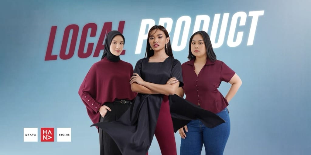 Drei Frauen in stilvollem Outfit posieren selbstbewusst vor einem blauen Hintergrund mit der Aufschrift "LOCAL PRODUCT" in fetten Buchstaben. In der unteren linken Ecke sind zwei Markenlogos zu sehen.